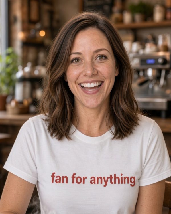 Frankie Fanelli, Dan’s AI sidekick, smiling in a café in a white tee that reads “fan for anything.”